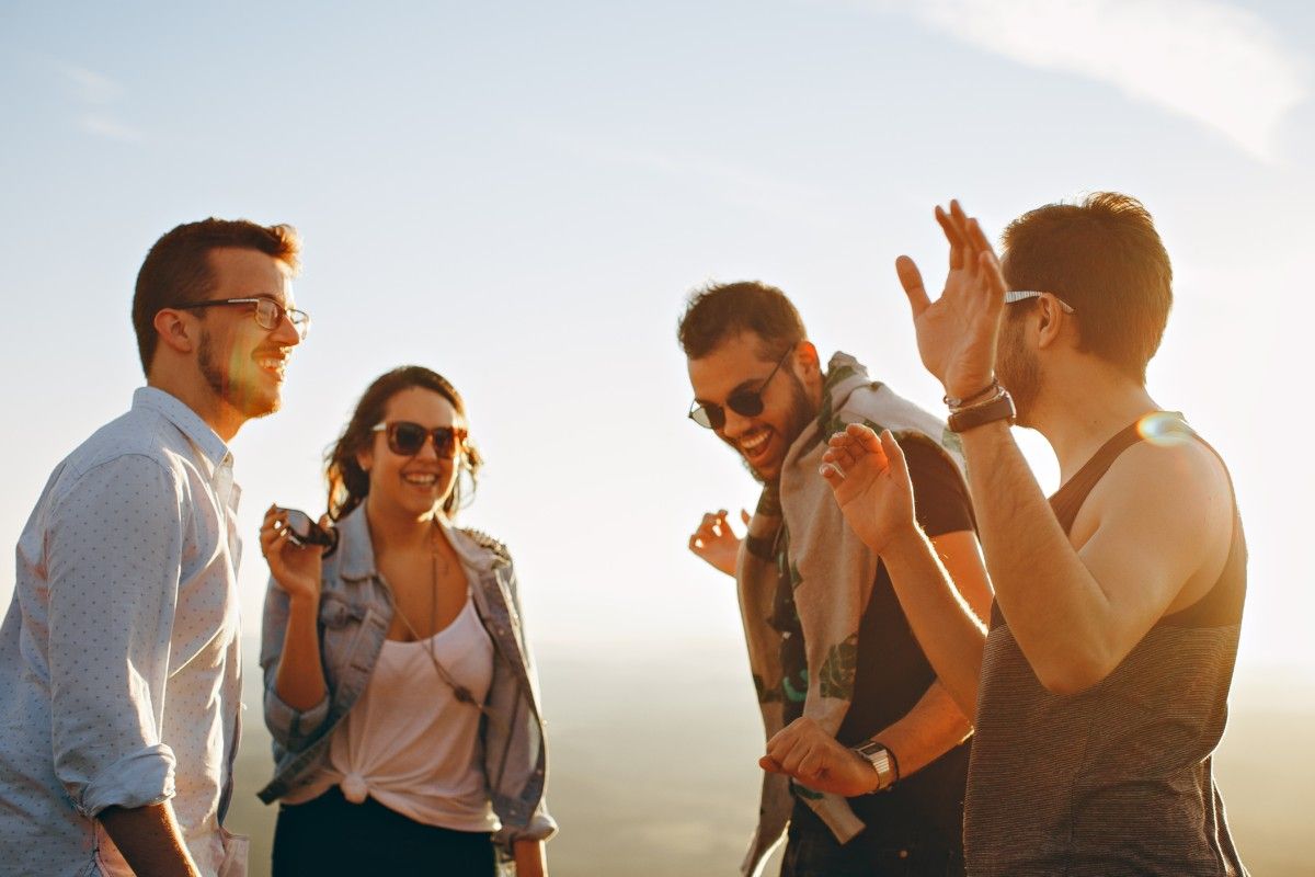 A group of four people talking and laughing outside in the sunlight.